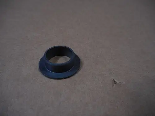 Schwarzes, rundes Bauteil mit einem Loch in der Mitte und einem abgesetzten Rand, abgebildet auf einem braunen Untergrund. Möglicherweise Zubehör von Remeha.